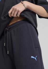 Marineblå joggers med snoretræk i taljen, ribbede manchetter, sidelommer og broderet lyseblå Puma-logo på venstre lår.