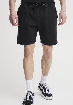 Sort bomuldsblandede shorts med en ribbet tekstur, der har en justerbar snøre i taljen og sidelommer. Båret med sorte sneakers og hvide sokker.