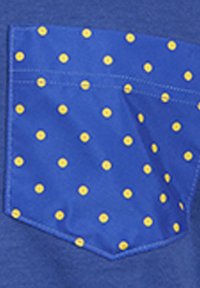 Blauer Stoff mit einer Tasche, die ein gelbes Punkte-Muster aufweist. Die Tasche hat eine geometrische Form und saubere Nähdetails.