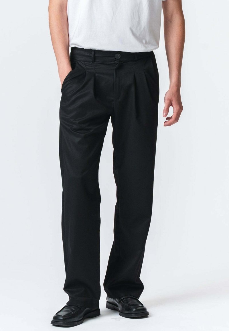 Sorte plisserede bukser i glat stof med knaplukning og to sidelommer. Sæt med sorte dressko.