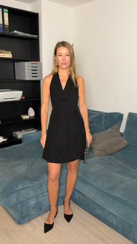 Czarna sukienka na szyję z drapowanym dekoltem, dopasowaną talią i rozkloszowanym dołem. Noszona z czarnymi, spiczastymi szpilkami, trzymając małą kopertówkę.