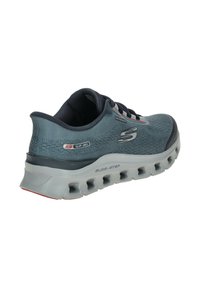 Chaussure de sport Skechers bleu-gris slip-on avec une tige en mesh respirant, une semelle blanche rembourrée avec des aérations glide-step, et une étiquette imperméable.