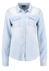 Ljust blå denimskjorta med knäppning, två bröstfickor och långa ärmar. Har en spetsig krage och en rundad nederkant.