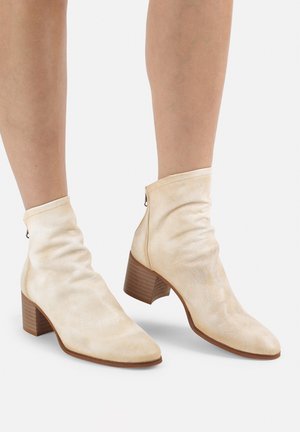 Cremfarbene Stiefeletten mit einem lässigen Design, spitzem Zehenbereich und 5 cm Blockabsatz. Glatte Struktur mit einem dezenten Glanz.