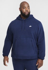 Felpa Nike blu navy con cappuccio, tasca a marsupio, cappuccio con cordino e logo bianco sul petto. Tessuto morbido e vestibilità comoda.