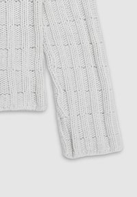 Gruby biały sweter z dzianiny, z teksturowanym wzorem podniesionych kwadratów. Rękawy wykończone są ściągaczami przy mankietach dla lepszej struktury.