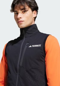Schwarze und orange Sportjacke mit hohem Kragen, durchgehendem Reißverschluss und strukturierten Mustern im unteren Bereich, mit dem Branding "TERREX".