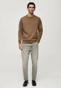 Felpa marrone con scollo tondo, jeans grigi a tapered e scarpe nere. Tessuto morbido, vestibilità rilassata e design minimalista.