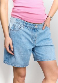 Helesinised teksapüksid, millel on klassikaline viie taskuga disain, nupuga kinnitamine ja sirge lõige tagataskutega.