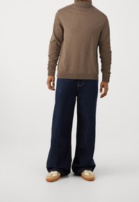 Brun polotröja i mjukt tyg. Kombinerad med vida mörk denimjeans. Skorna har beige och bruna accenter med en sportig design.