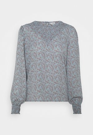 Blouse bleu clair avec un motif floral brun et vert. Présente un col smocké et de longues manches bouffantes avec des poignets froncés.