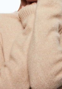 Maglione beige realizzato in morbido materiale a maglia, con un collo alto e maniche testurizzate, dal taglio rilassato.