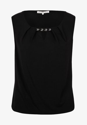 Kobieta idąca, ubrana w czarny top bez rękawów, ciemne obcisłe jeansy, beżowe baleriny i niosąca beżową torbę na ramię.