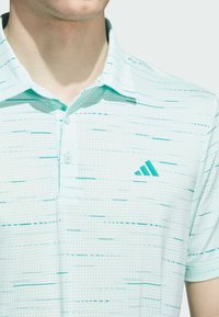 Polo shirt azzurro chiaro con un motivo testurizzato caratterizzato da sottili linee orizzontali. Include un collo e un logo ricamato sul petto.