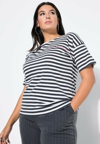 Pruhované tričko v námořnické modři a bílé, s krátkými rukávy, kulatým výstřihem, s růžovým textem na hrudi, kombinované se šedými pruhovanými kalhotami.