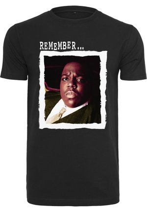 Sort t-shirt med et fremtrædende grafik af en mand med en alvorlig mine, indrammet af en hvid, rivet papirstil kant. Teksten lyder "HUSK...".