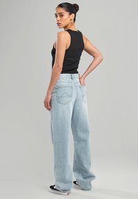 Light blue wide-leg jeans with a high waist, featuring back pockets and minimal stitching detail, paired with a black sleeveless top.