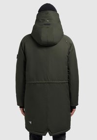 Grøn parka med polstret design, høj krave og aftagelig hætte. Indeholder trykknapper og en side-logo-patch.