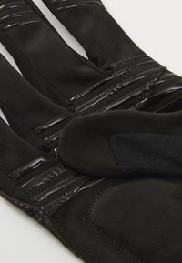 Sorte hansker laget av et mykt, teksturert materiale. Med blanke sorte detaljer og flere sydd linjer langs toppen.