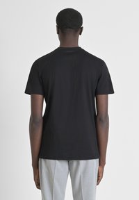 Camiseta negra de manga corta y cuello redondo. Textura suave, diseño ajustado, con un detalle de logo cerca del cuello en la parte posterior.