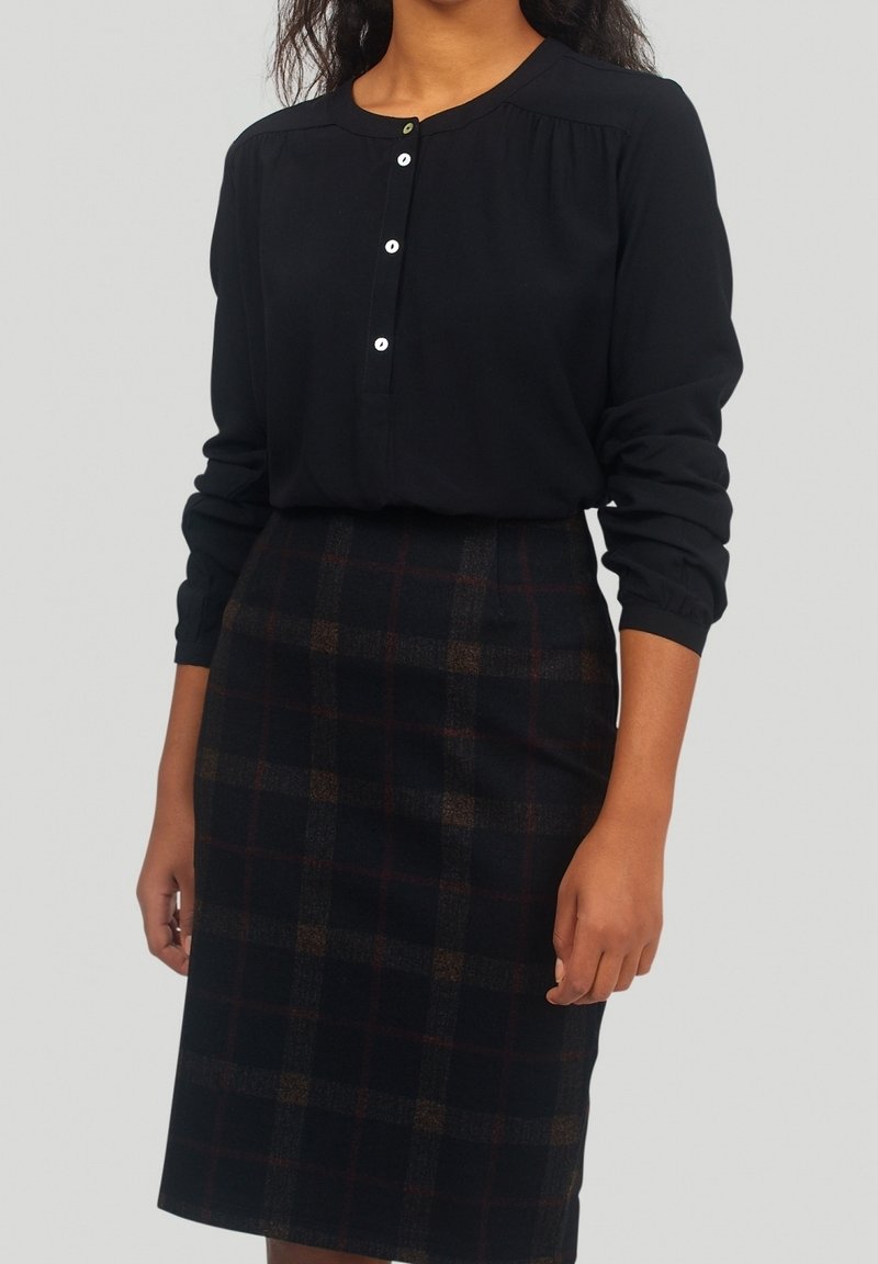 Svart långärmad blus med detaljerade knappar, kombinerad med en knälång pennkjol i mörk rutigt mönster i brunt och marinblått.