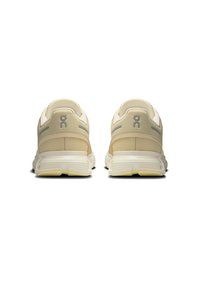 Zapatos deportivos beige con diseño de malla, soporte trasero y logo visible. Detalles texturizados y suela ligera de goma.