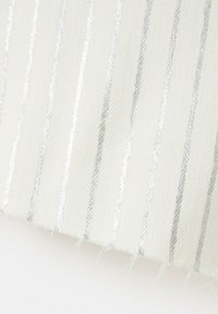 Tissu blanc avec des rayures verticales argentées brillantes et des bords légèrement effilochés sur un fond blanc uni.