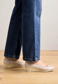 Beige wedge shoes with a ribbed texture, featuring a woven jute accent on the sole. Paired with dark blue wide-leg jeans.