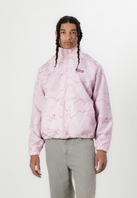 Pink jacket with a wave pattern, featuring a high collar and zip closure. Elastic cuffs and hem, paired with light blue jeans.