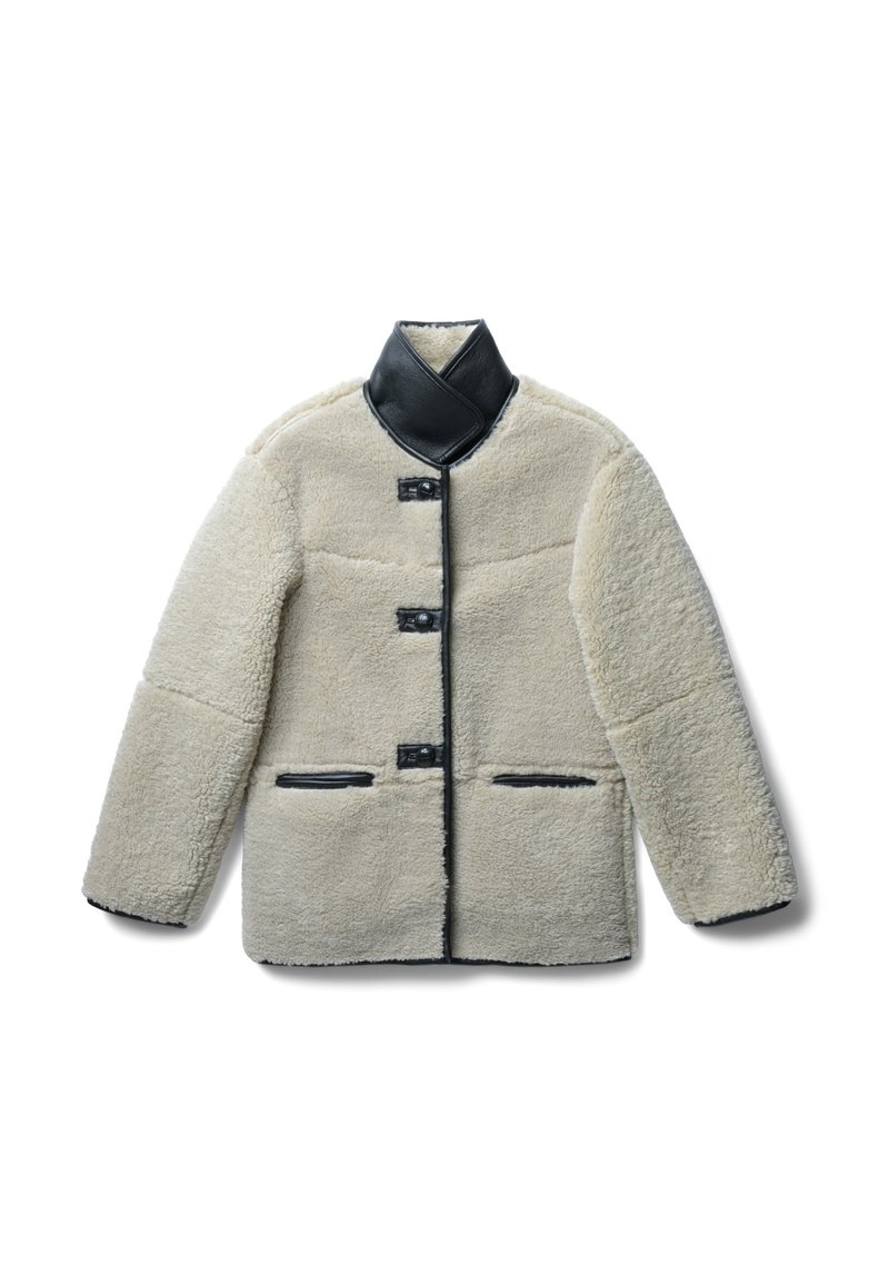 Cremefarbene Lammfelljacke mit einem schwarzen Lederkragen, die vier Knöpfe und schwarze Lederakzente an den Taschen aufweist.