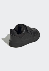 Scarpa sportiva nera con tomaia in pelle liscia, dettagli in rete, cinturino in velcro e suola in gomma testurizzata. Design minimalista con tre strisce.