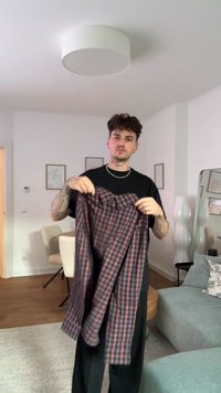 Camisa de manga longa em padrão xadrez, azul-marinho com riscas vermelhas, com gola abotoada e bolso no peito, segurada por uma pessoa vestindo roupa casual.
