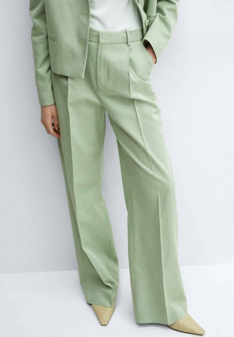 Pantalon large vert clair en tissu texturé, avec des plis devant et des poches latérales, associé à un haut ajusté clair et des escarpins beiges à bout pointu.