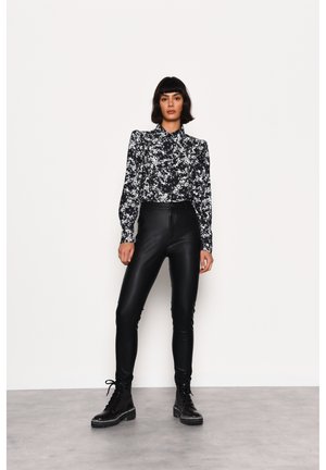 Sort-hvid blomsterbluse med krave-design, parret med højtaljede sorte læderbukser og sorte snørebåndsstøvler.