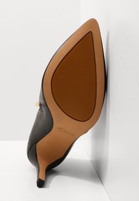 Scarpa con tacco alto in pelle nera con punta a spillo, suola marrone chiaro e marchio discreto sulla suola. Texture liscia.