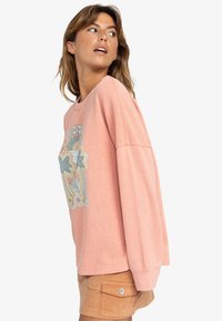 Hellrosa Langarm-Sweatshirt mit strukturierter Oberfläche, das auf der Vorderseite einen lebhaften Grafikdruck mit Palmblättern und Blumen aufweist.