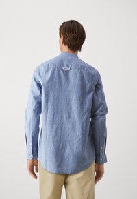 Camisa azul claro de algodón, con cuello abotonado, mangas largas y una textura sutil, con una etiqueta en la parte posterior.