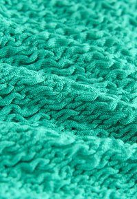 Tissu tricoté turquoise avec un motif de torsades ondulées et en relief, créant des plis texturés et de la profondeur.