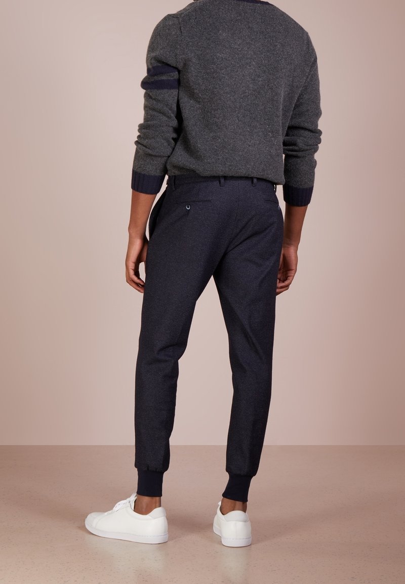 Šedý svetr s námořnickými akcenty, kombinovaný s tmavě námořnickými zúženými kalhotami a bílými teniskami. Viditelná vlněná textura, přiléhavý střih.