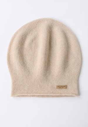 Berretto lavorato a maglia beige in morbida lana, caratterizzato da un motivo testurizzato e un piccolo marchio etichetta nella parte inferiore. Parte superiore arrotondata senza cuciture visibili.