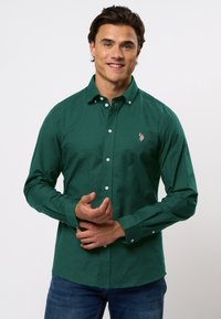 Zöld gombos ing, pamutból készült, gallérral, hosszú ujjal, és egy kis hímzett díszítéssel a bal mellen.