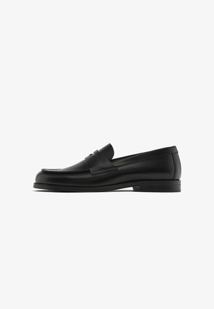 Black leather loafers with a rounded toe, stitching details, and a decorative leather strap across the vamp; flat rubber sole.