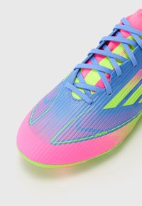 Bright pink and blue soccer shoe with a textured upper, featuring green accents and a gradient design, secured by light blue laces.