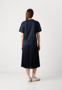 Navy T-shirt and pleated skirt from behind, textured fabric, soft drape, paired with light sneakers and beige socks. Simple, clean design.