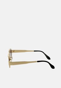 Złote okulary przeciwsłoneczne z cienkimi ramkami, przezroczystymi noskami i czarnymi końcówkami zauszników; soczewki mają delikatny gradient od jasnego do ciemnego.