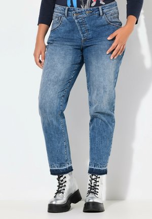 Jeans de tiro alto en azul claro con un corte relajado, que presentan un diseño clásico de cinco bolsillos y puños enrollados, combinados con botas plateadas de cordones.