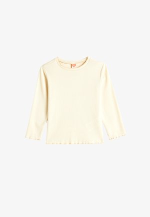 Langsleeve, crèmekleurig shirt van ribstof. Heeft een ronde halslijn en zoom met een subtiele golvende textuur. Geen opvallende accenten.