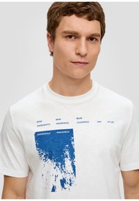 Biała bawełniana koszulka z krótkim rękawem z niebieskim graficznym wzorem, z napisem zawierającym "STEP", "INTO" i "BLUE". Okrągły dekolt.