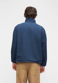 Σκούρο μπλε μπουφάν με γιακά όρθιο, κατασκευασμένο από υφασμάτινη υφή. Διαθέτει άνετη εφαρμογή και μακριά μανίκια. Ορατές ραφές στους ώμους και μανσέτες.