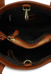 Wnętrze brązowej skórzanej torebki z czarnymi paskami, kieszonka na zamek, akcenty ze złotego metalu i pętla do zawieszania breloka.